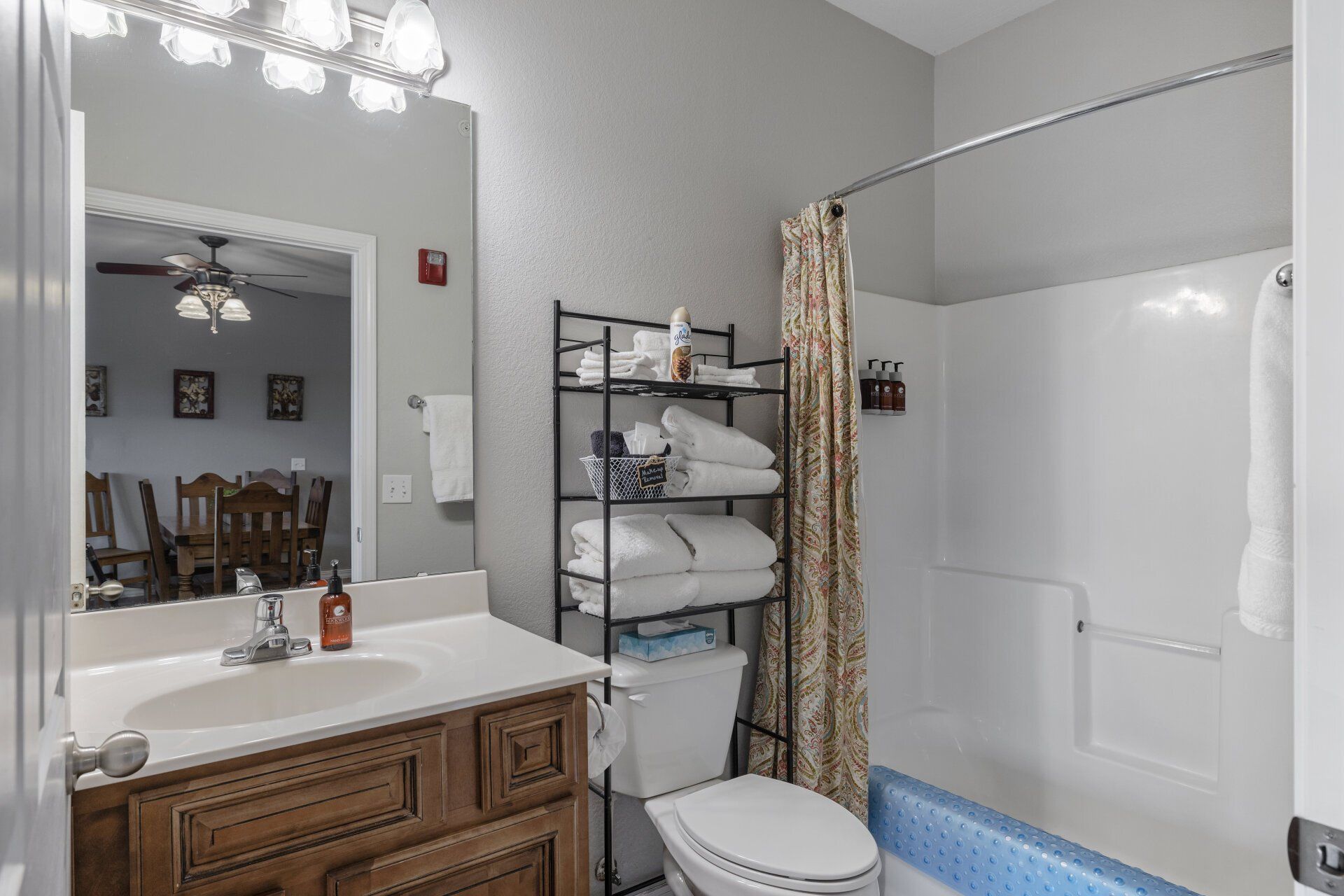 Bathroom with vanity, mirror, shelving, toilet, shower curtain, and white tub with blue trim