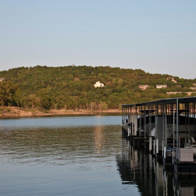 Calm lake with a wooded hillside and docked covered boats at sunset