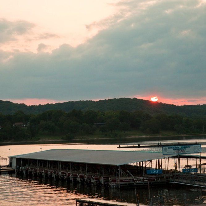 Sunset over a calm lake with a covered dock and silhouetted hills in the distance