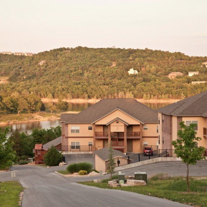Apartment buildings on a winding road with a wooded hill and lake in the background