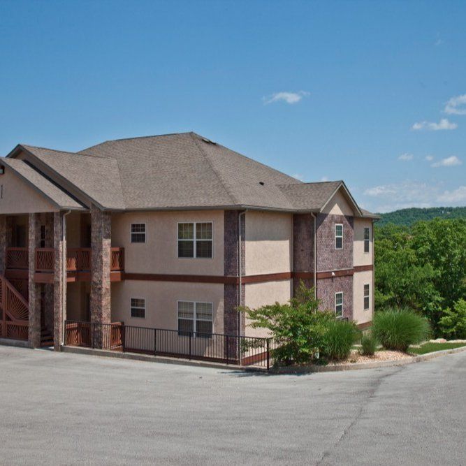 Apartment building with beige siding and red brick trim beside a paved driveway under a blue sky