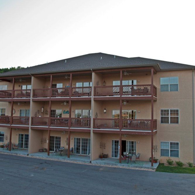 Three-story apartment building with balconies, red railings, and a sloped dark roof.