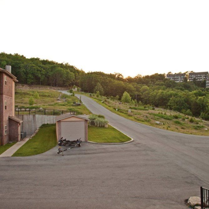 Quiet paved road curving past grassy hills, trees, and a small shed at dusk
