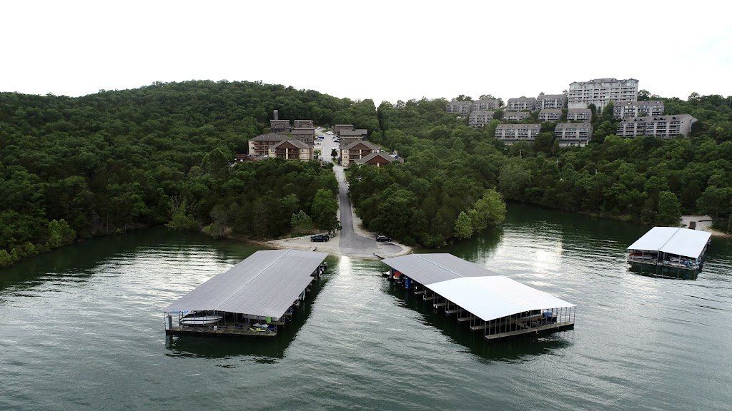 Docked boats on a calm lake below a tree-covered hillside with buildings in the distance