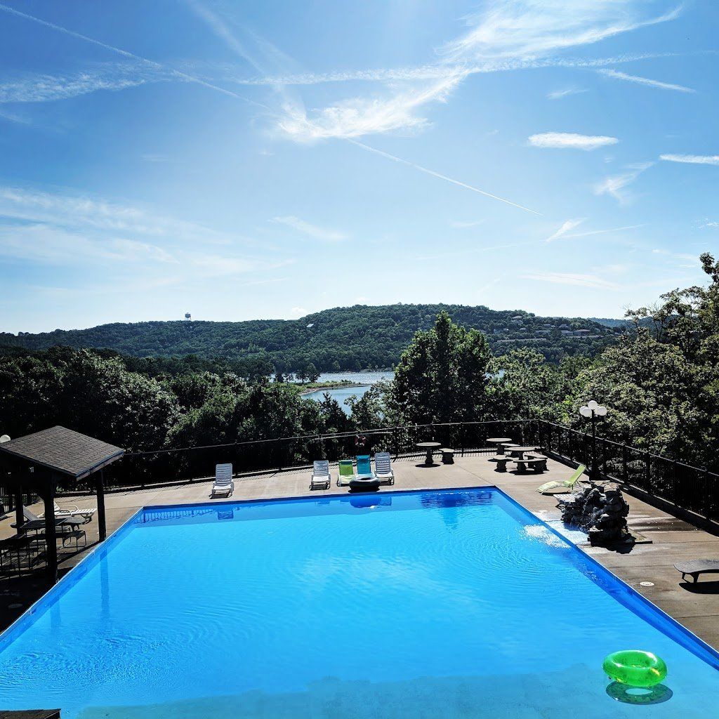 Blue swimming pool overlooking a lake and green hills under a clear sky