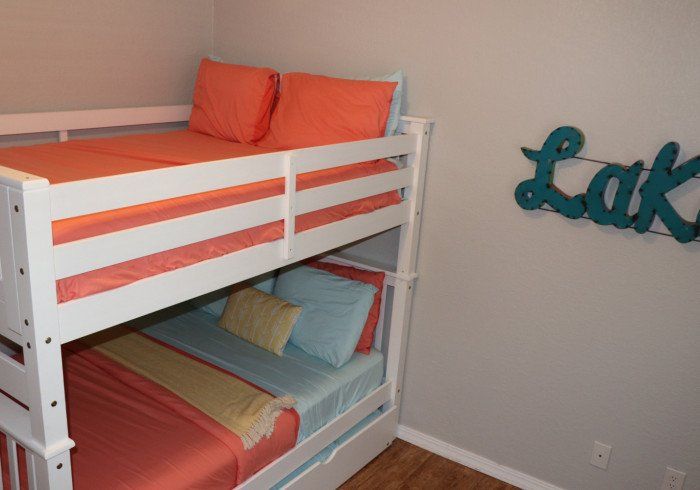 White bunk bed with orange and blue bedding in a small room, beside teal wall letters