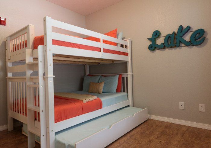 White bunk bed in a child’s room with coral bedding and teal wall decor reading “Lake”