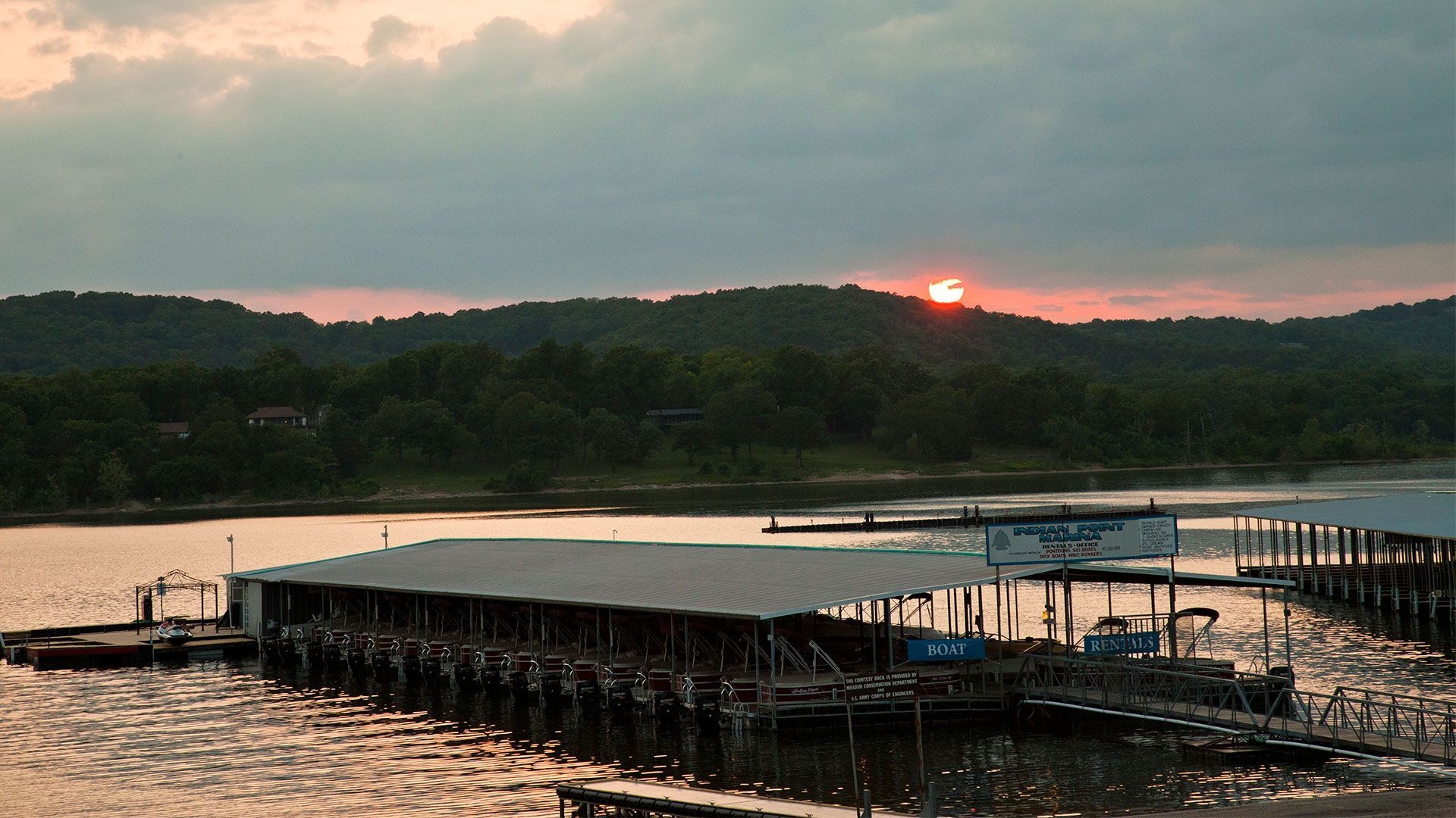 Sunset over a calm lake with a dock and covered boat slips in the foreground