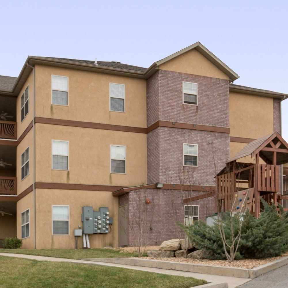 Three-story tan apartment building with brown accents and exterior stairway