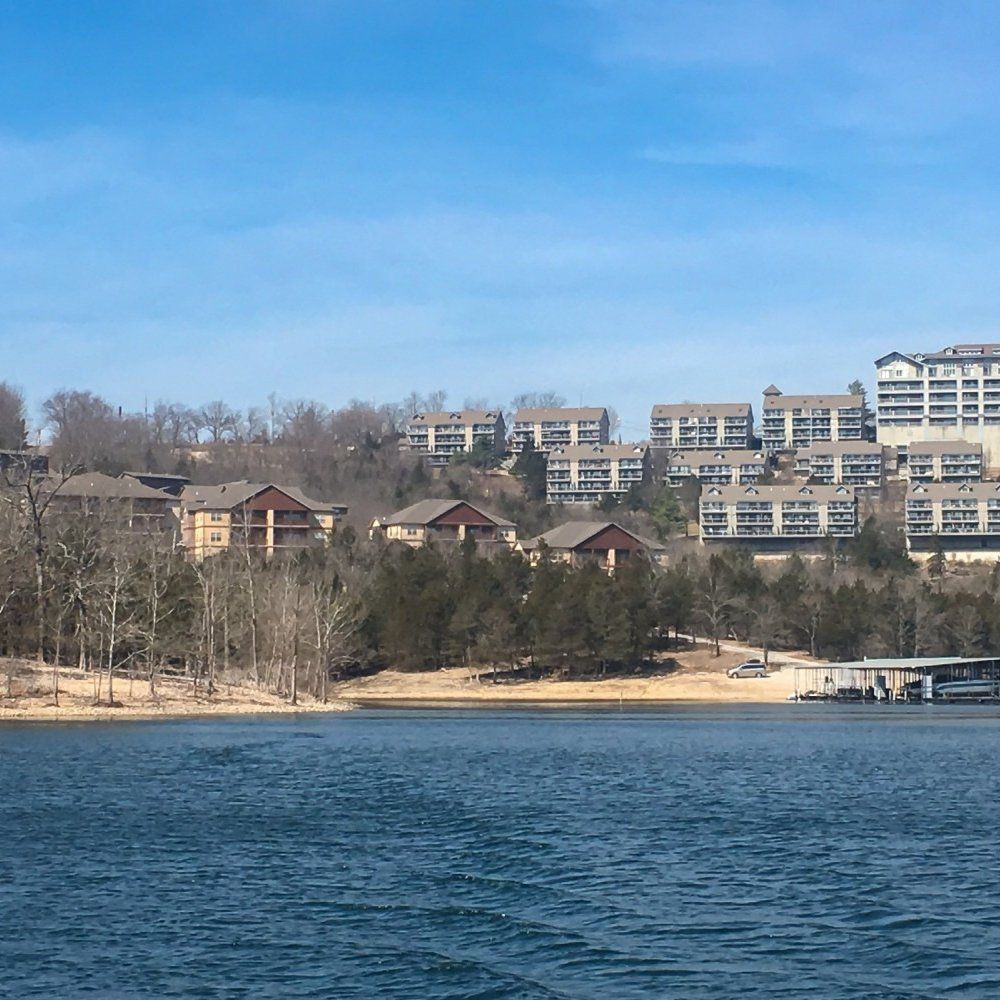 Lakeside resort buildings above a sandy shore with blue water in the foreground under a clear sky