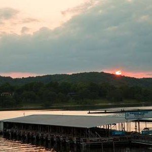 Sunset over a calm river with a dock and tree-covered hills in the distance