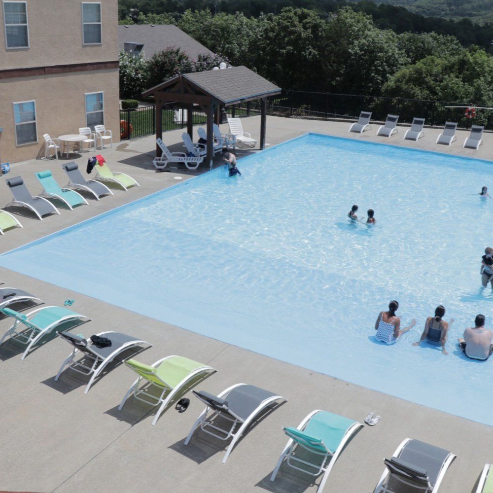 Outdoor swimming pool with a few people relaxing and swimming, lounge chairs along the deck, and a shaded cabana.