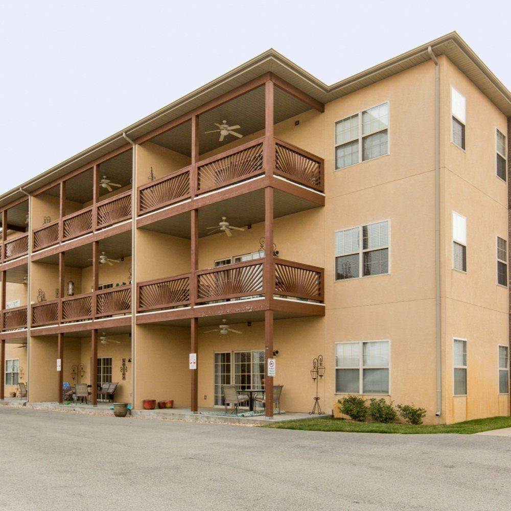 Three-story tan apartment building with brown balconies and a gravel parking area