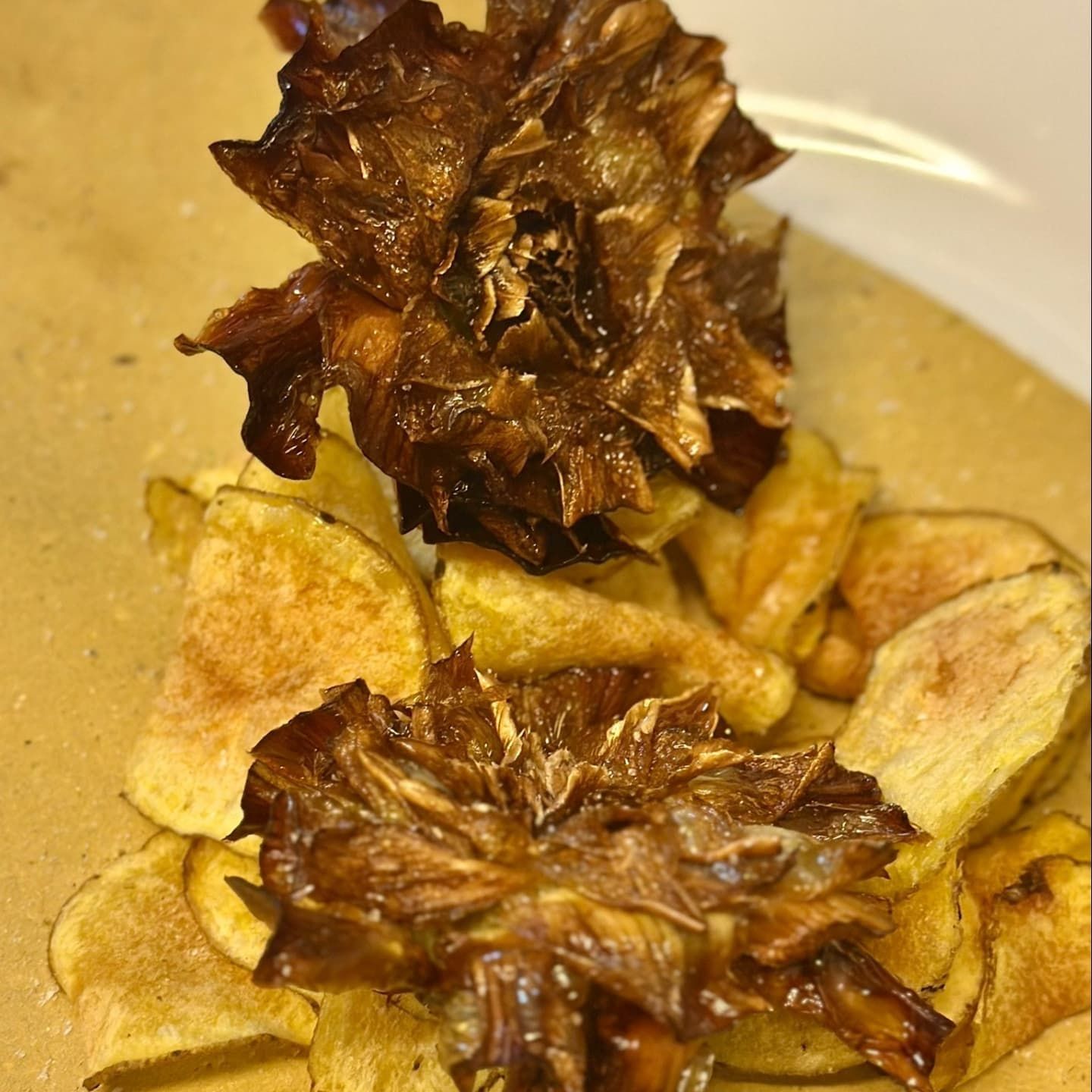 Fiori di carciofo croccanti su patatine fritte, disposti su una superficie marrone chiaro.