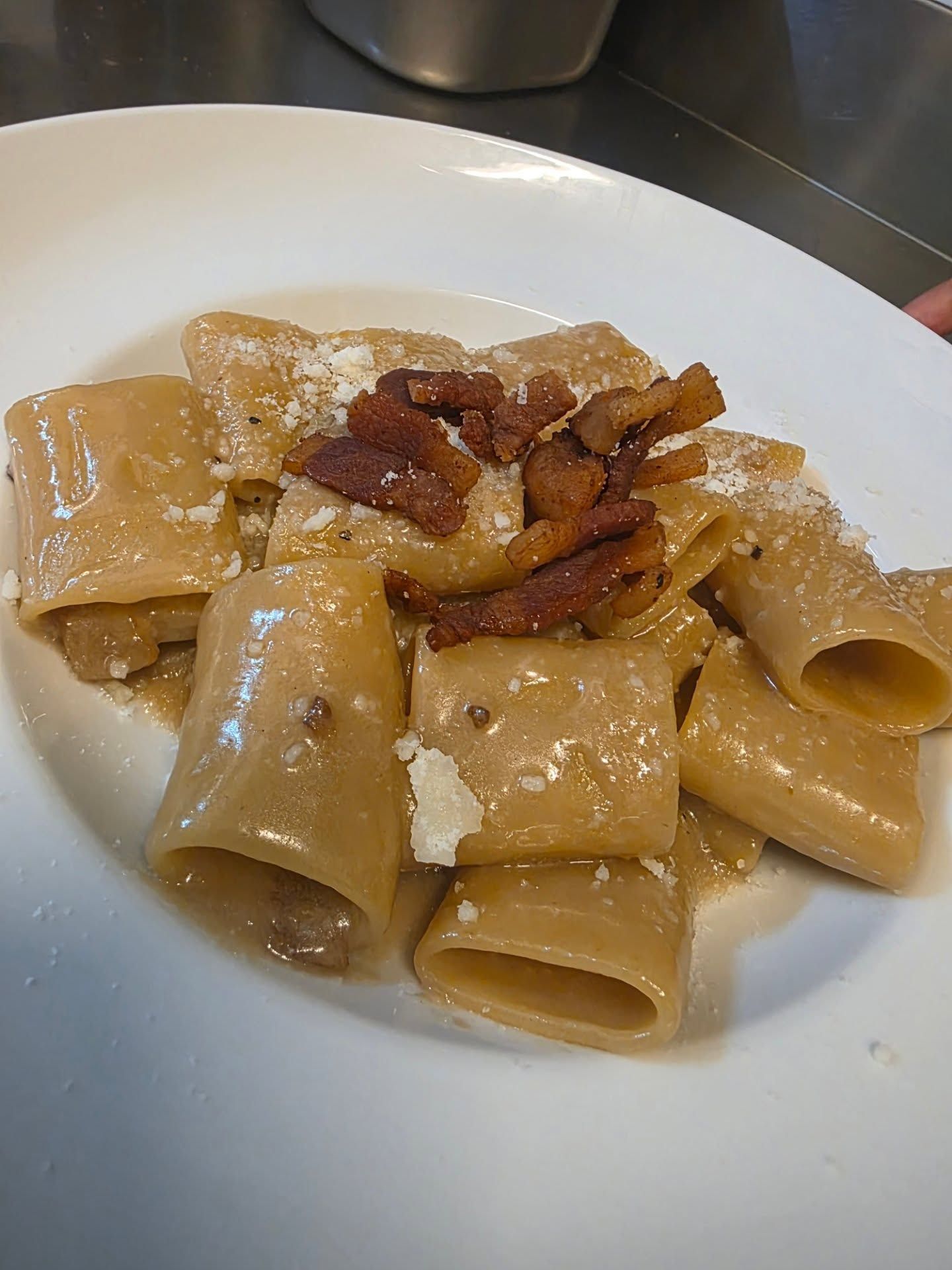 Pasta alla carbonara: rigatoni spessi in salsa cremosa, conditi con pancetta croccante e formaggio grattugiato, serviti su un piatto bianco.