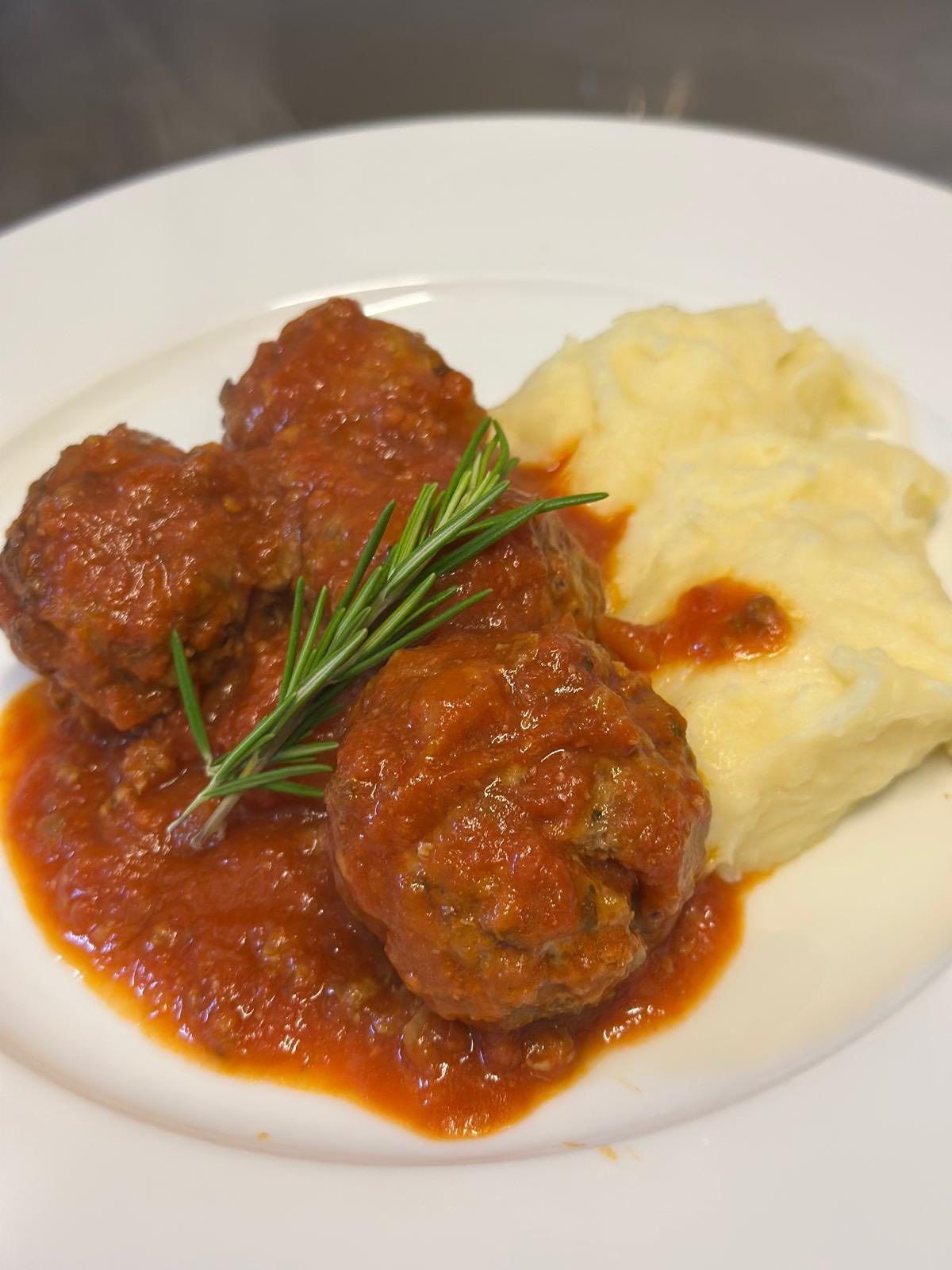 Polpette in salsa di pomodoro con purè di patate e guarnizione di rosmarino.