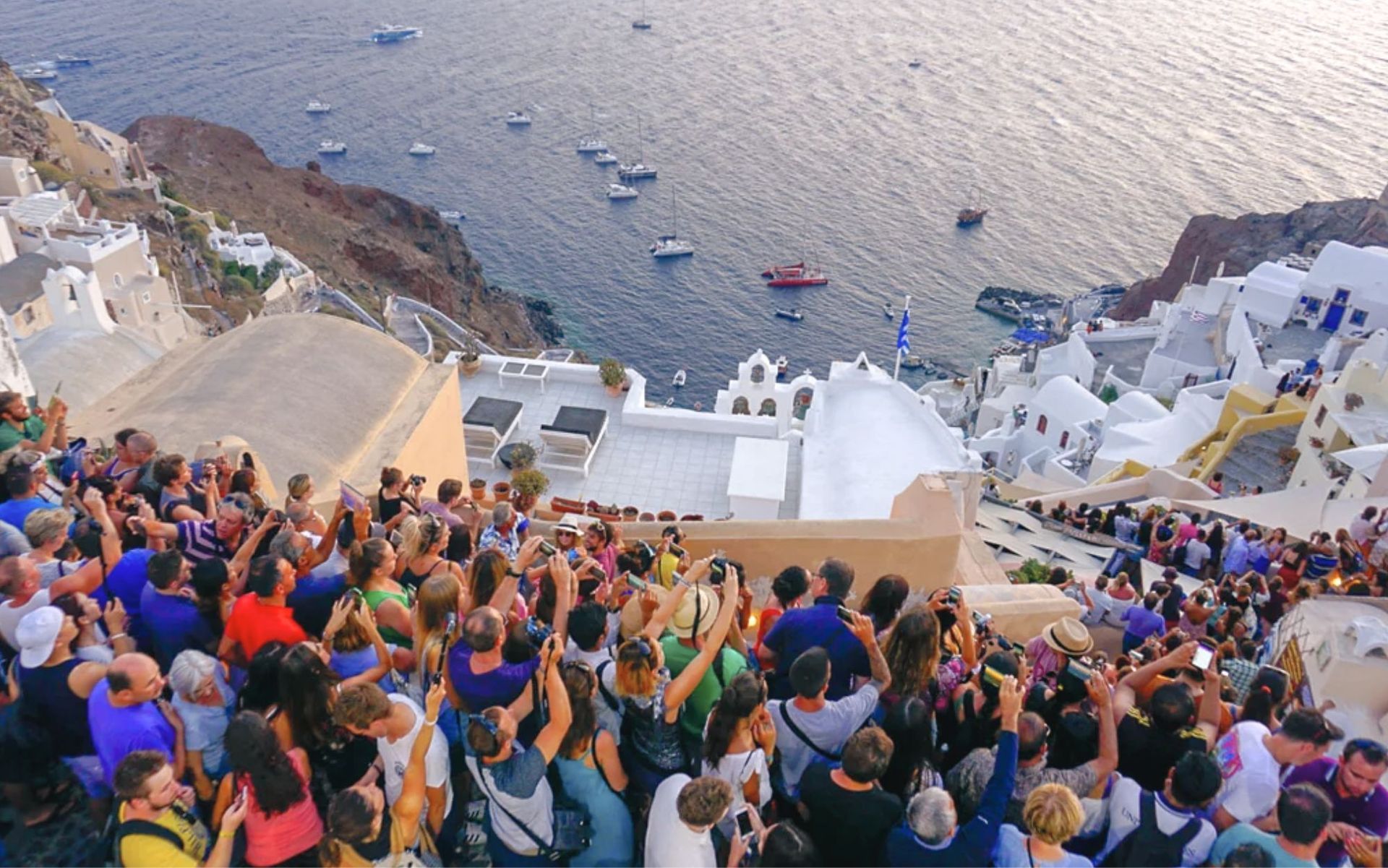 Sunset crowds in Oia, Santorini, with visitors gathered along the caldera viewpoint and whitewashed village rooftops