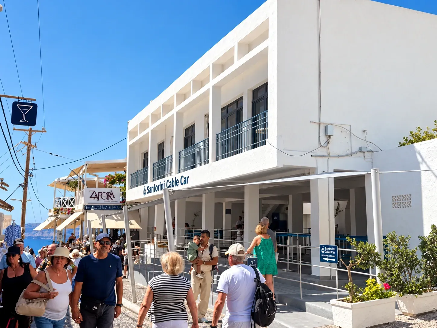 Visitors outside the Santorini Cable Car entrance in Fira on a sunny day.