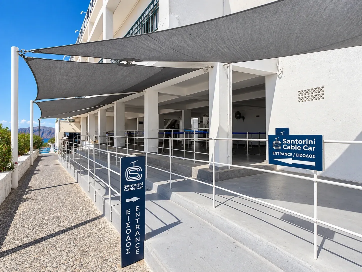 Santorini Cable Car entrance in Fira with directional signs and shaded waiting lanes.