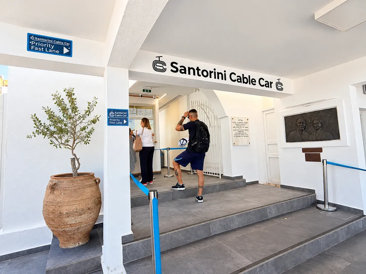 Santorini Cable Car entrance in Fira with Priority Fast Lane signs and travelers waiting inside.