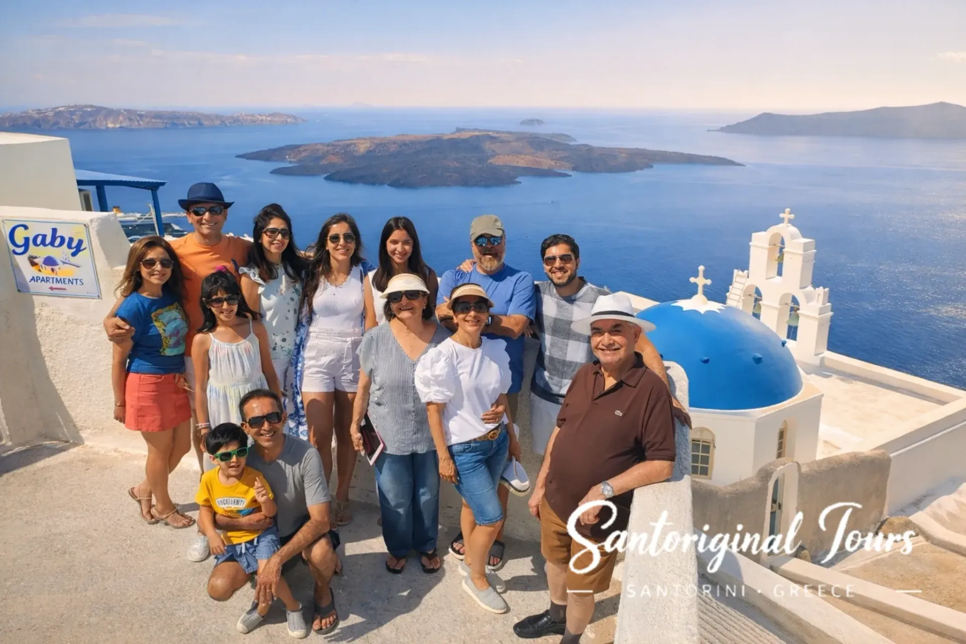 Multigenerational family posing in Santorini with a blue dome church, bell tower, and caldera view in the background