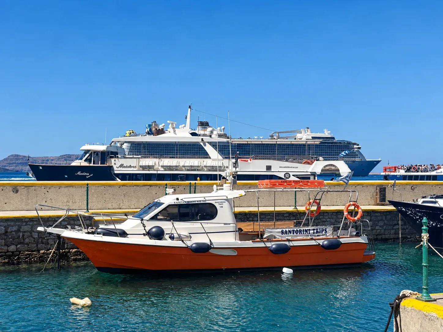 Water taxi, tender boat, and cruise ship at Santorini Old Port in Fira.
