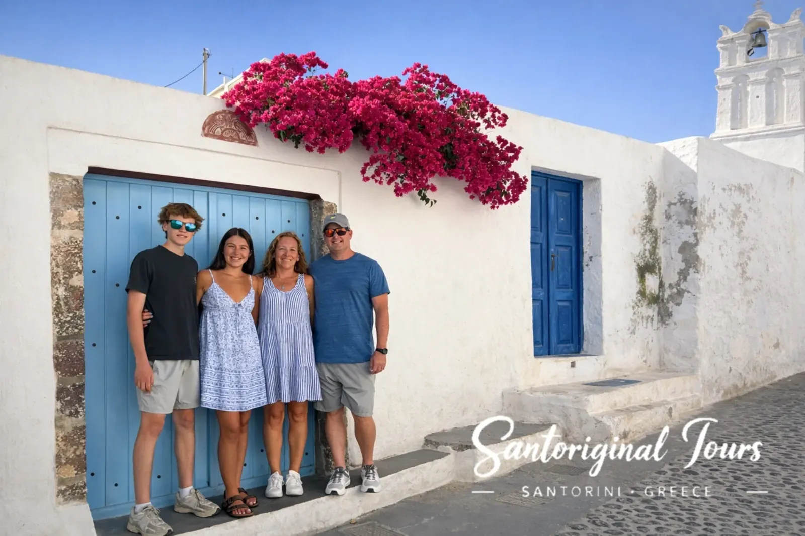 Family of four posing in Santorini by a blue door and bright bougainvillea during their private tour