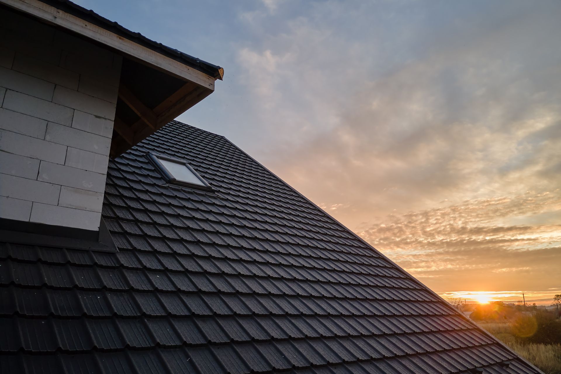 Rooftop with dark shingles and skylight at sunset, with orange clouds on the horizon