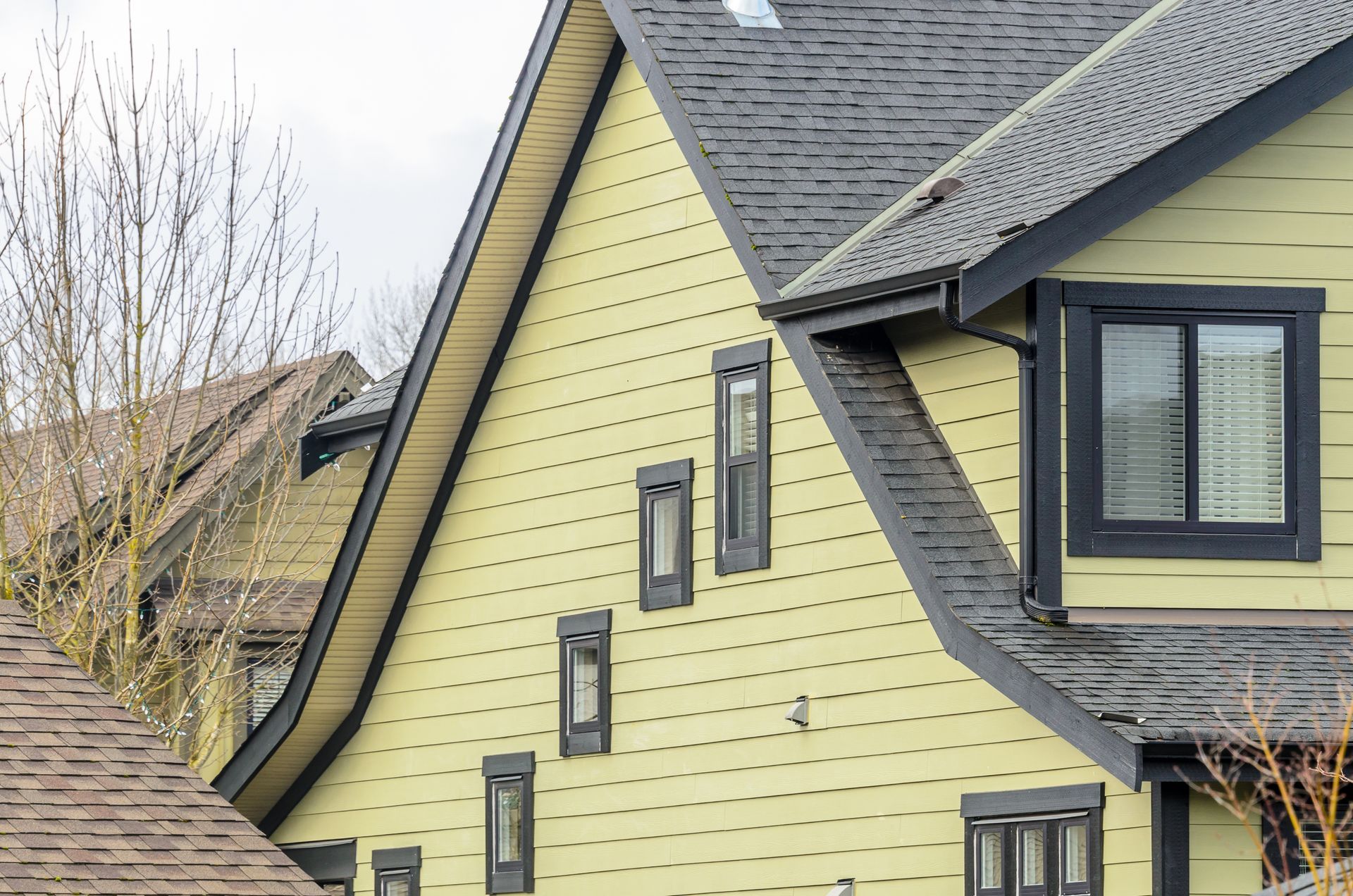 Yellow house with steep gray roofs and black-trimmed windows, viewed from the side