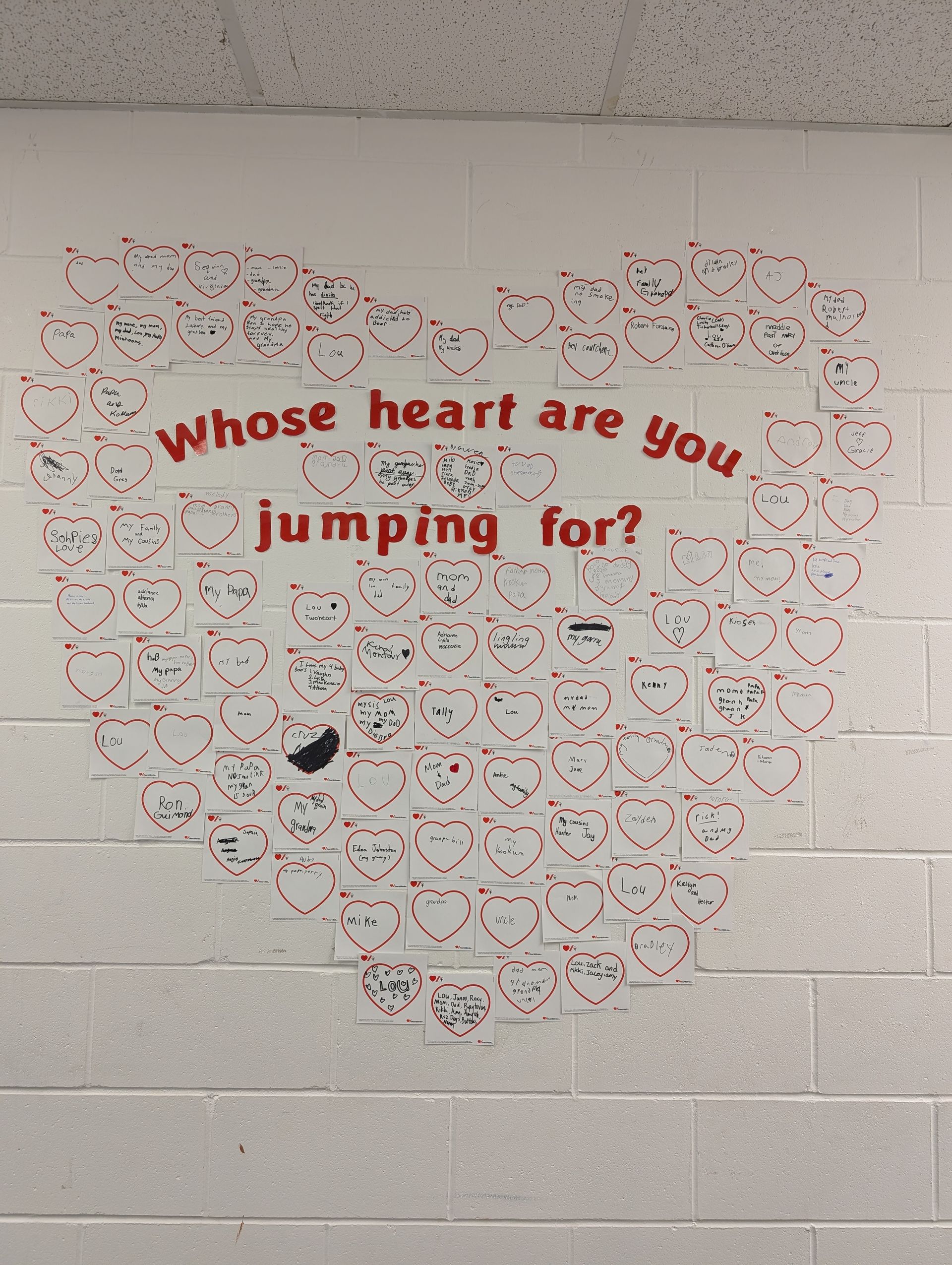 A mural of paper hearts on a school wall that says, “whose heart are you jumping for?”