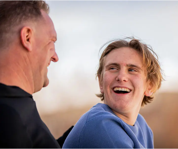 Max and Mike sitting outside looking at each other laughing.