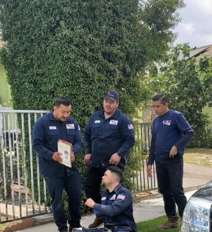 Four police officers in navy uniforms stand and sit by a fence in a residential area, one holding a folder.