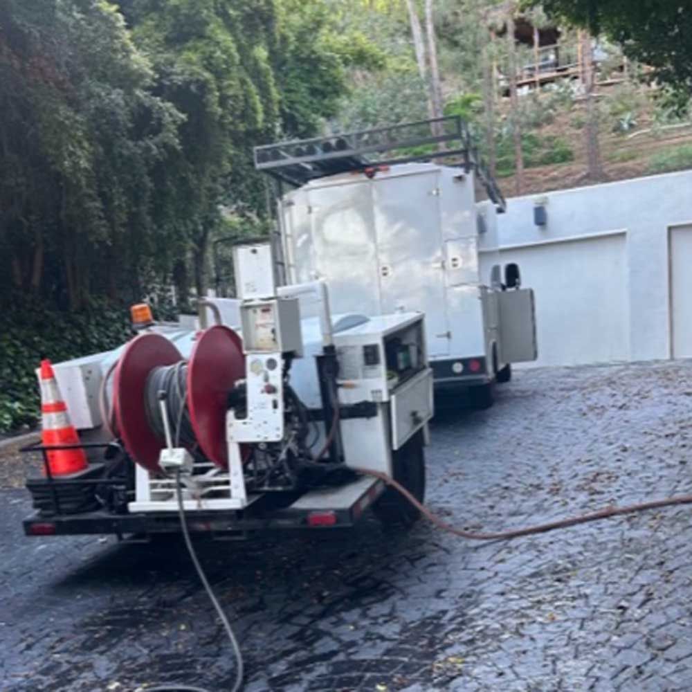 Utility truck with hose reels and equipment parked on a wet driveway beside a garage during cleanup work