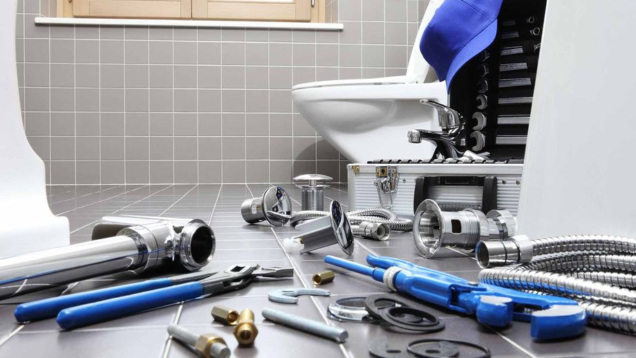 Bathroom repair tools scattered on a floor beside a toilet and tiled wall