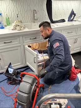 Plumber repairing a bathroom sink cabinet with tools and a drain snake on the floor