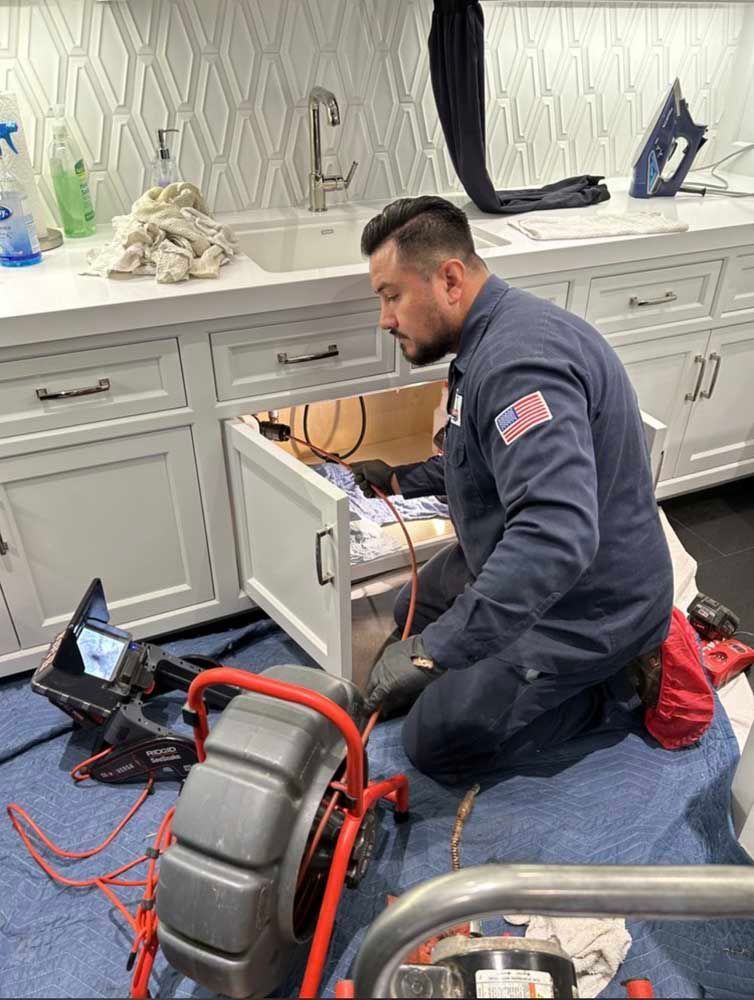 Plumber repairing a bathroom sink cabinet with tools and a drain snake on the floor