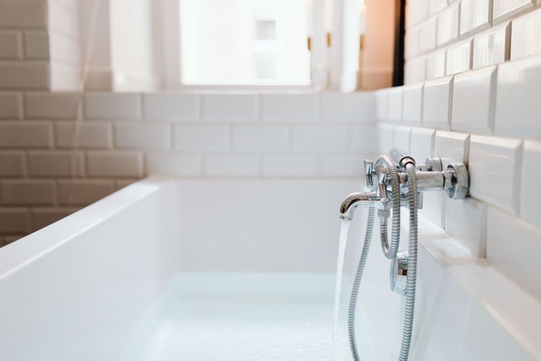 White bathtub with chrome faucet and shower hose in a bright tiled bathroom