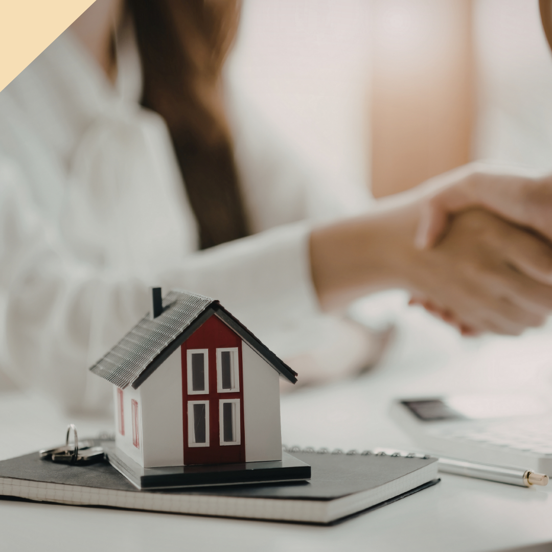 Miniature house on a notebook; people shake hands, real estate deal.