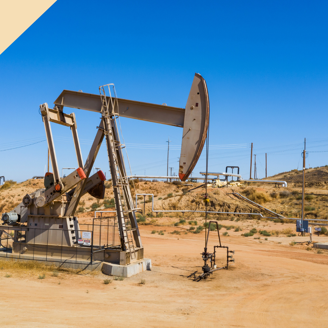 Oil pump jack in a dry, desert-like landscape under a clear blue sky.
