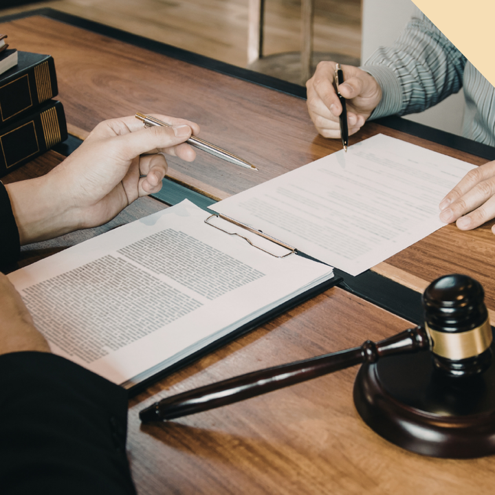 Two people at a desk review documents; a gavel rests on the table.