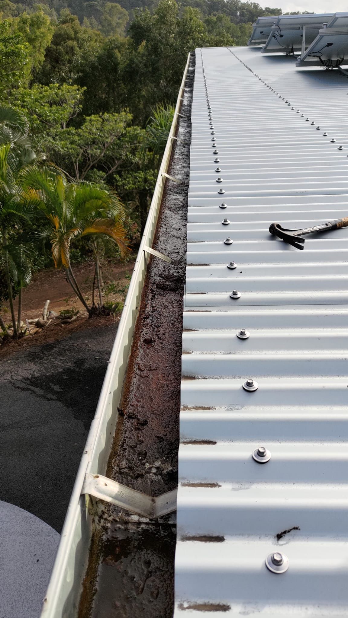 A Metal Roof Edge Next to a Gutter Filled With Debris — Rhettro Roofing Industry in Taroomball, QLD