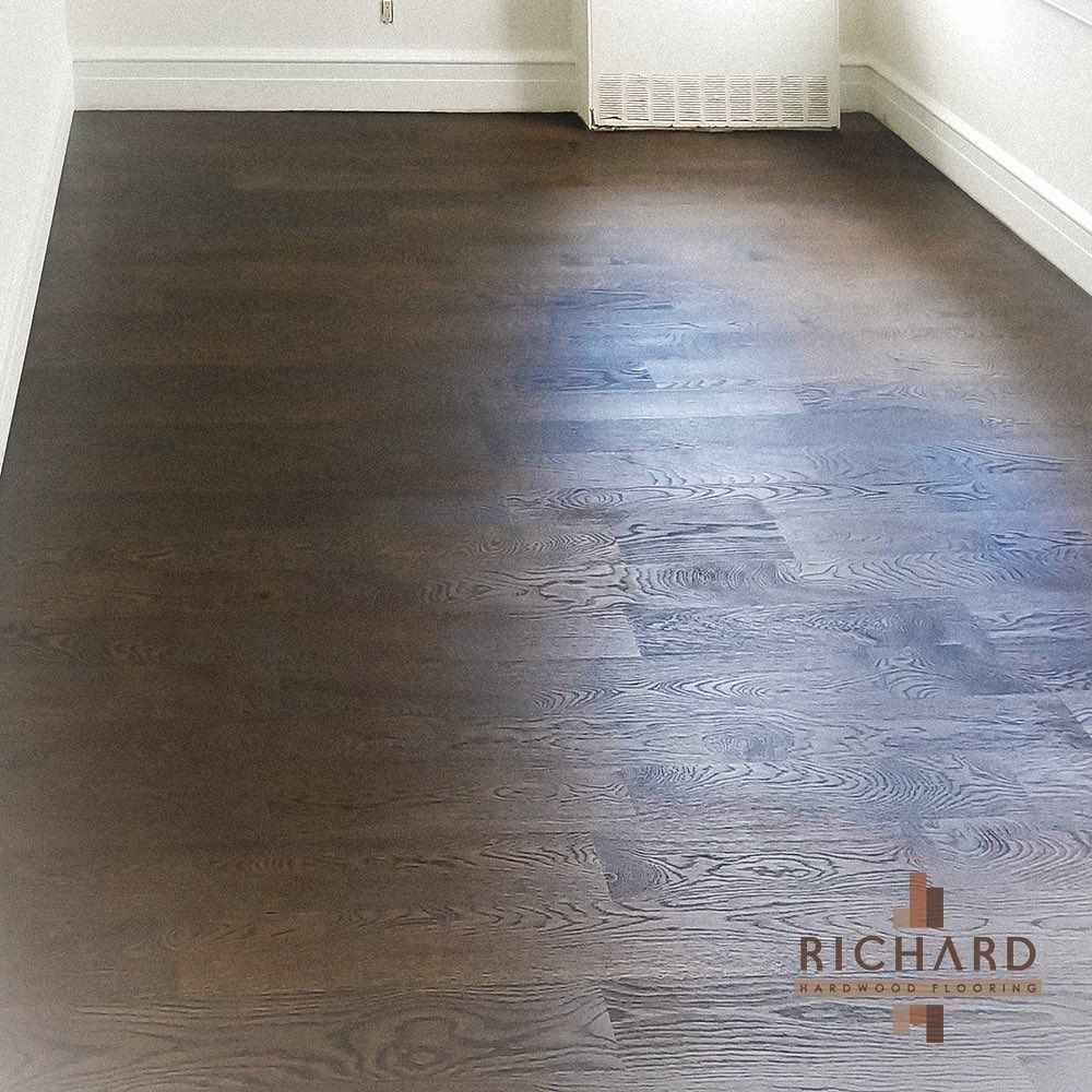 Dark-stained hardwood flooring installed in a room with white baseboards and a wall vent.