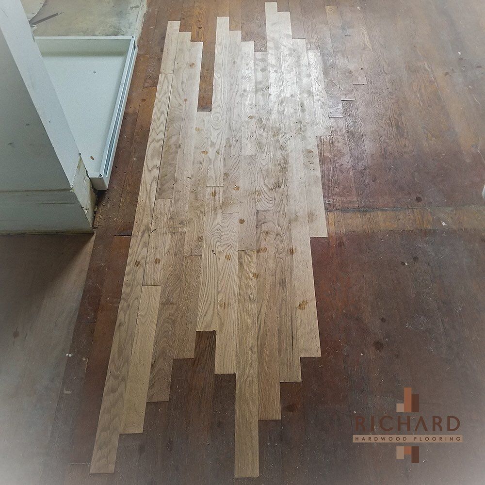 A strip of light-colored, unfinished hardwood floor is being installed within a darker, worn wooden floor area.