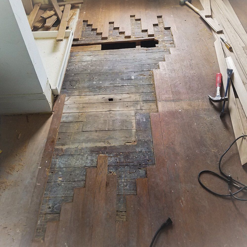Stair-stepped gaps in wood flooring reveal a dark subfloor, with tools and wooden planks placed to the side for repairs.