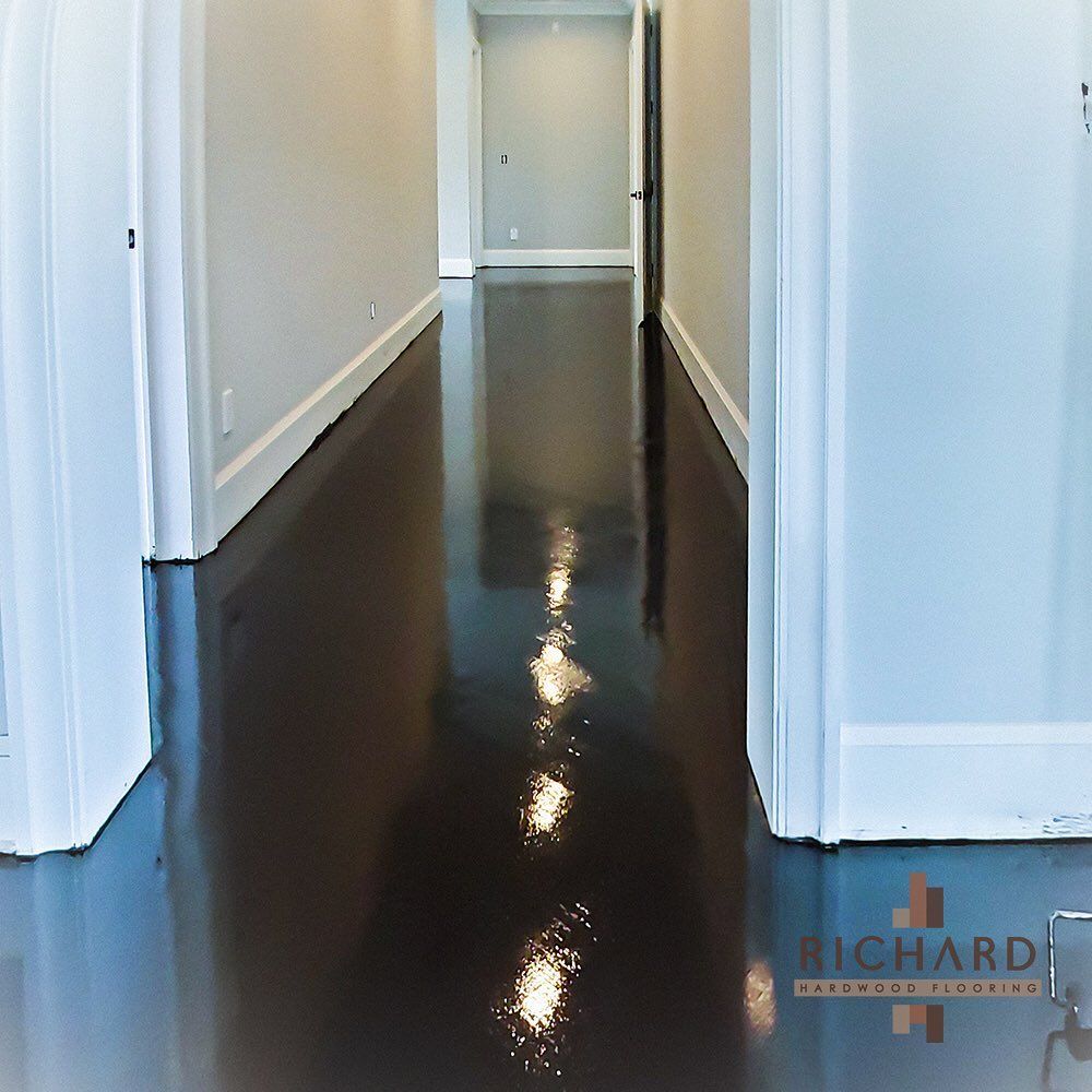 A hallway with a highly polished, dark floor reflecting bright light, leading to an open doorway.