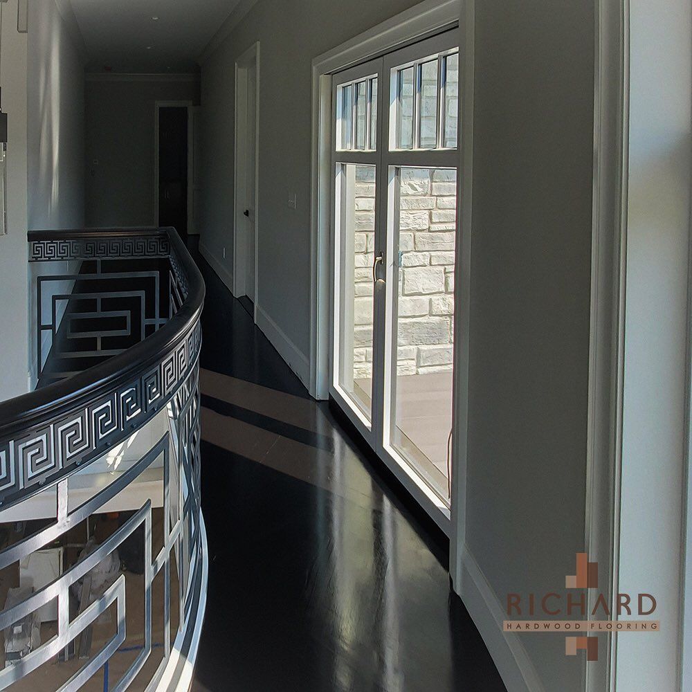 A hallway with dark hardwood floors, white walls, and a decorative metal railing overlooking a staircase.