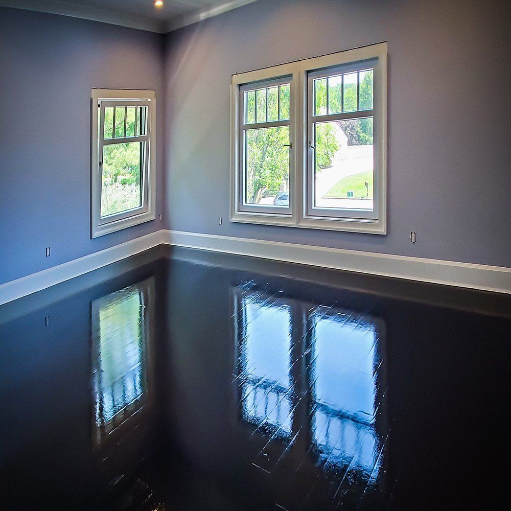 A room with lavender walls and white trim features a highly reflective, dark, polished floor mirroring the windows.