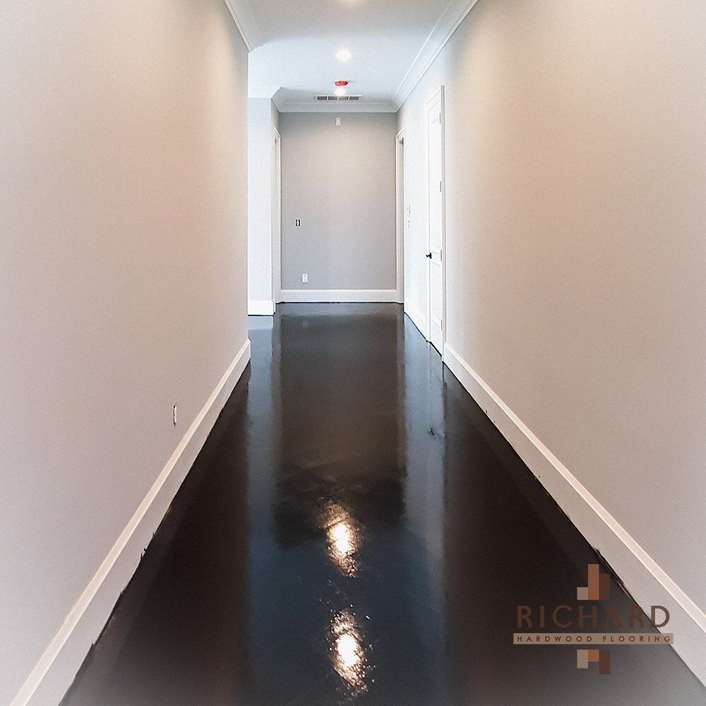 A bright, empty hallway with light gray walls, white baseboards, and a high-gloss, dark brown hardwood floor.