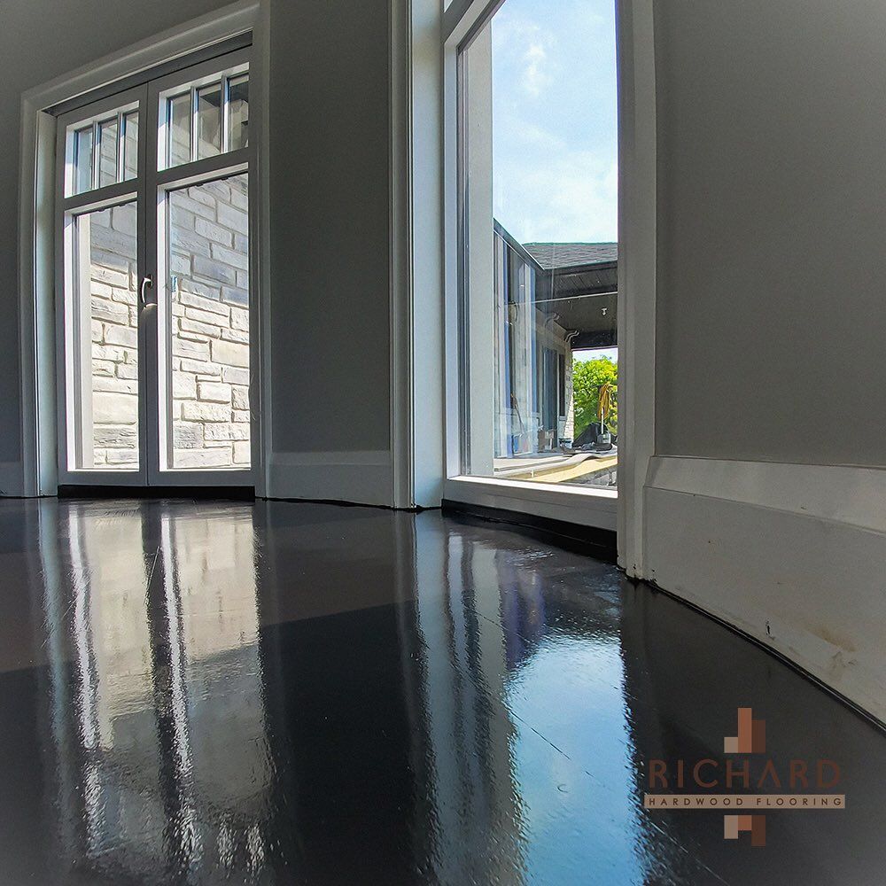 A view of a bright room with dark, high-gloss polished concrete flooring reflecting the windows and exterior scenery.