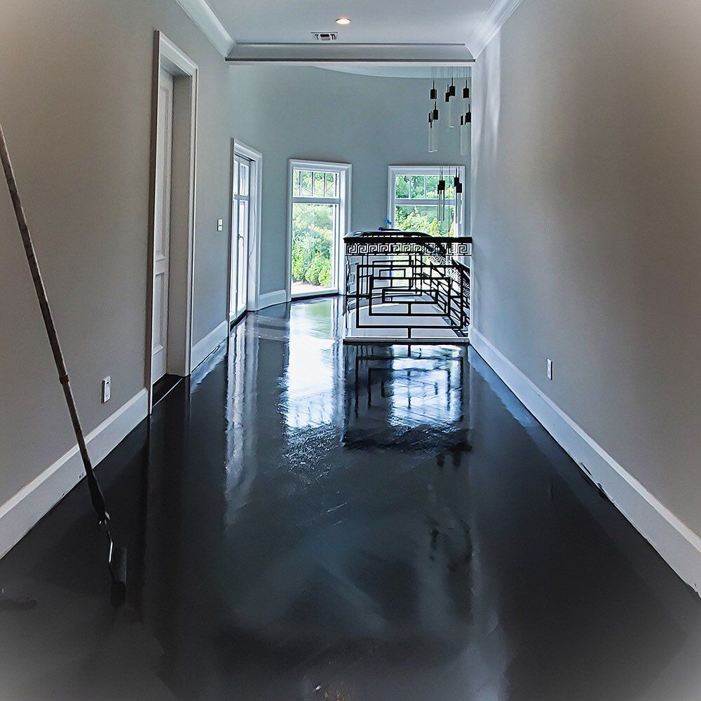A hallway with grey walls, white trim, and a high-gloss, dark-colored reflective floor, leading to a balcony railing.